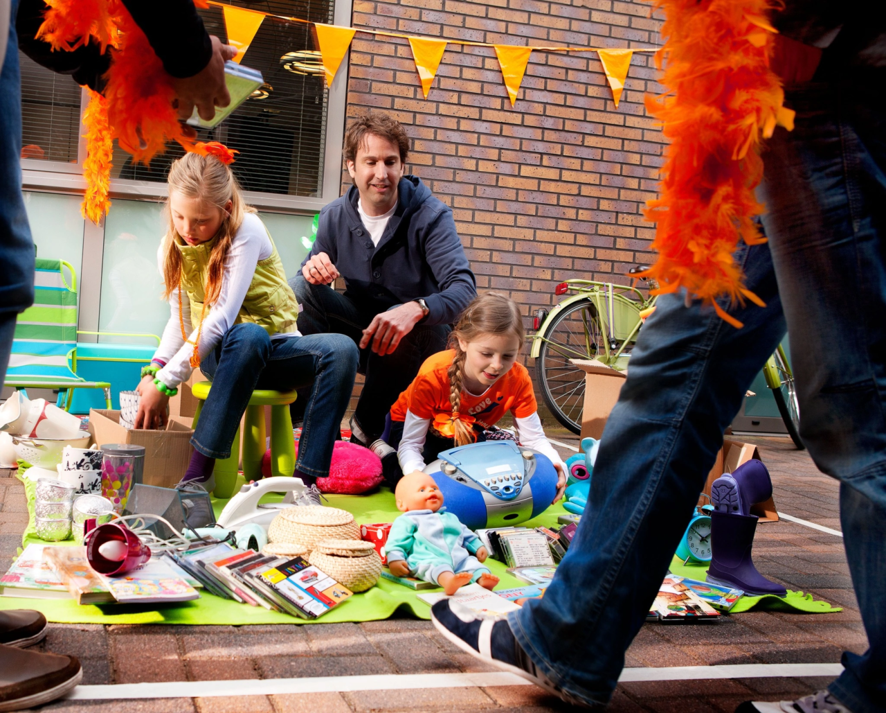 Twee meisjes en hun vader verkopen spullen op de vrijmarkt op Koningsdag.